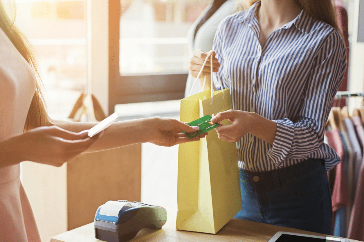 Woman with a green shopping bag paying a store employee with her credit card